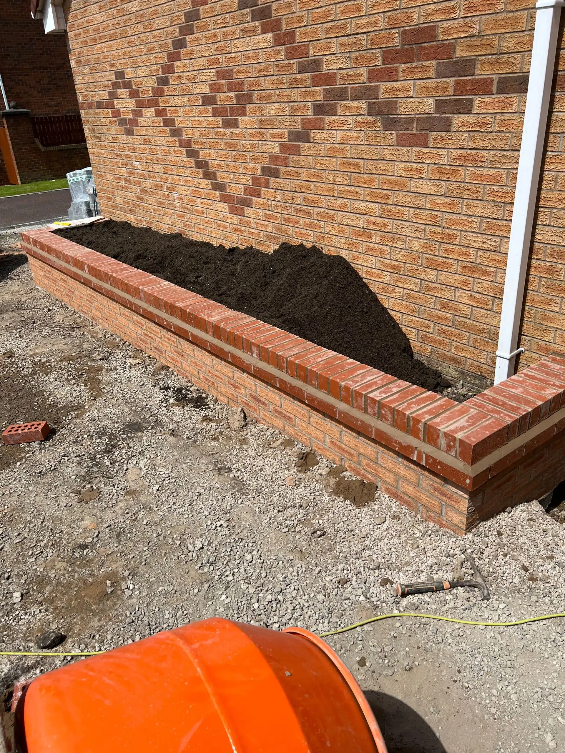 Brick raised garden bed filled with dark soil against house