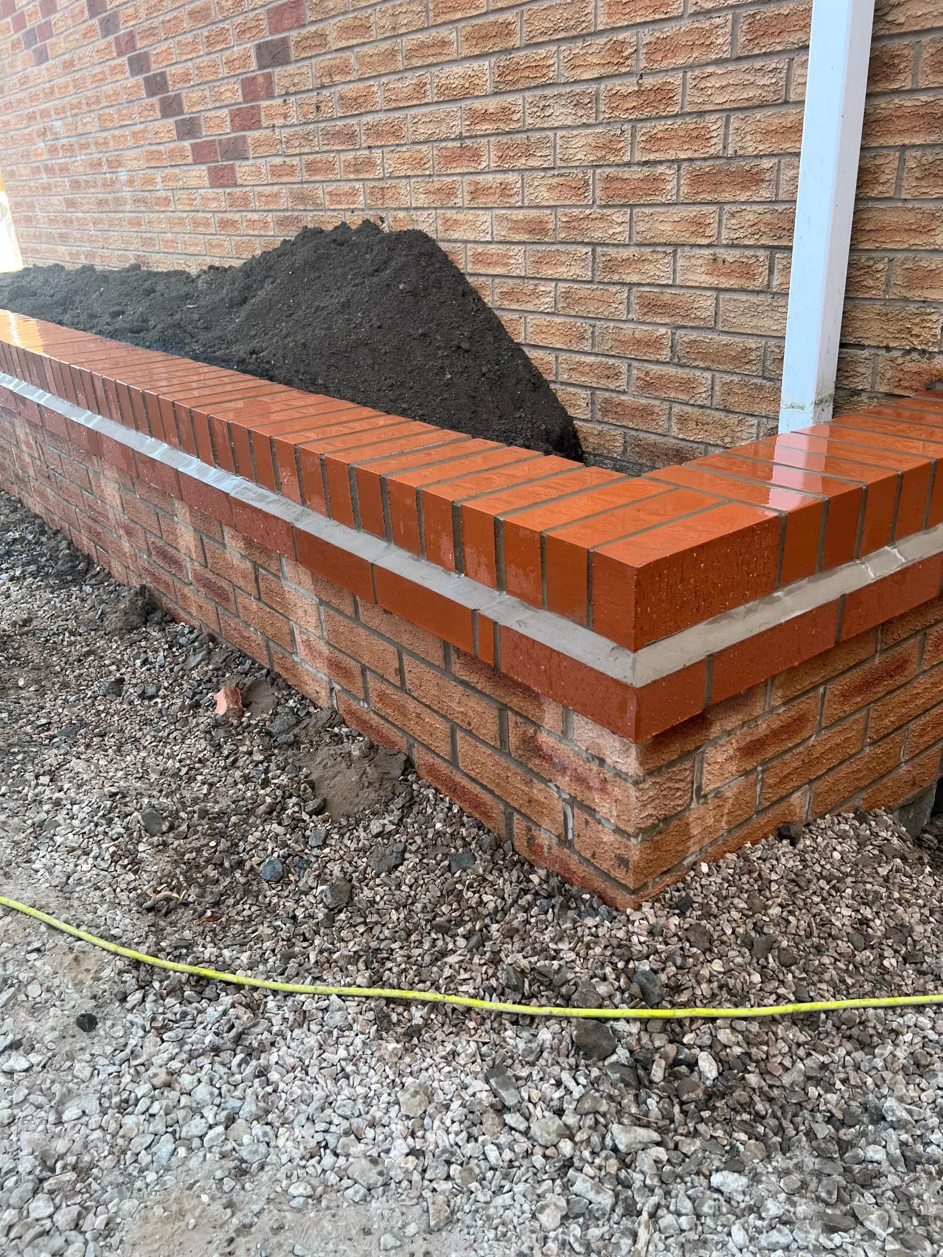 Brick planter box with dark soil against brick wall